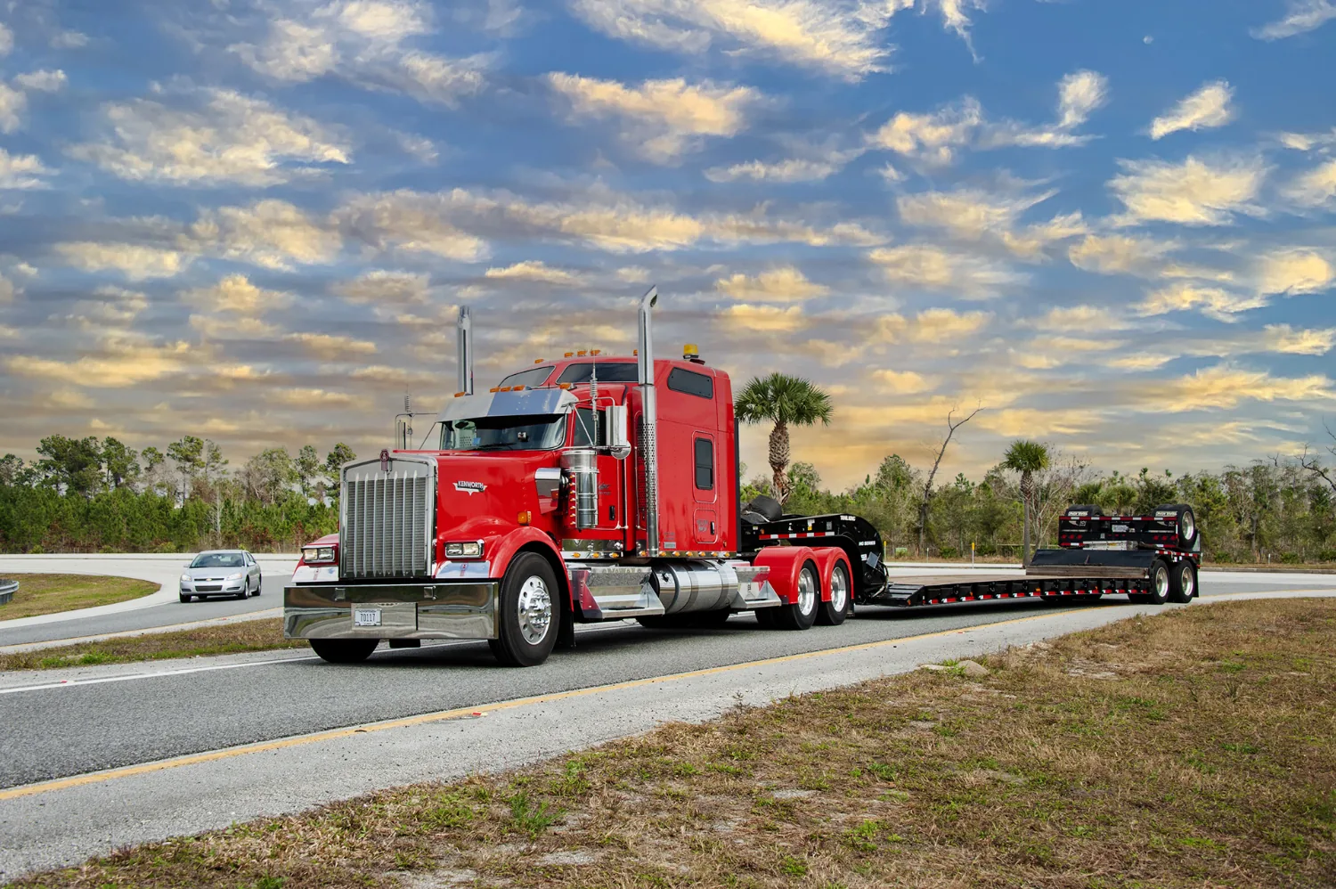 Red drop-bed heavy-haul trailer hauling an oversized load on the highway.